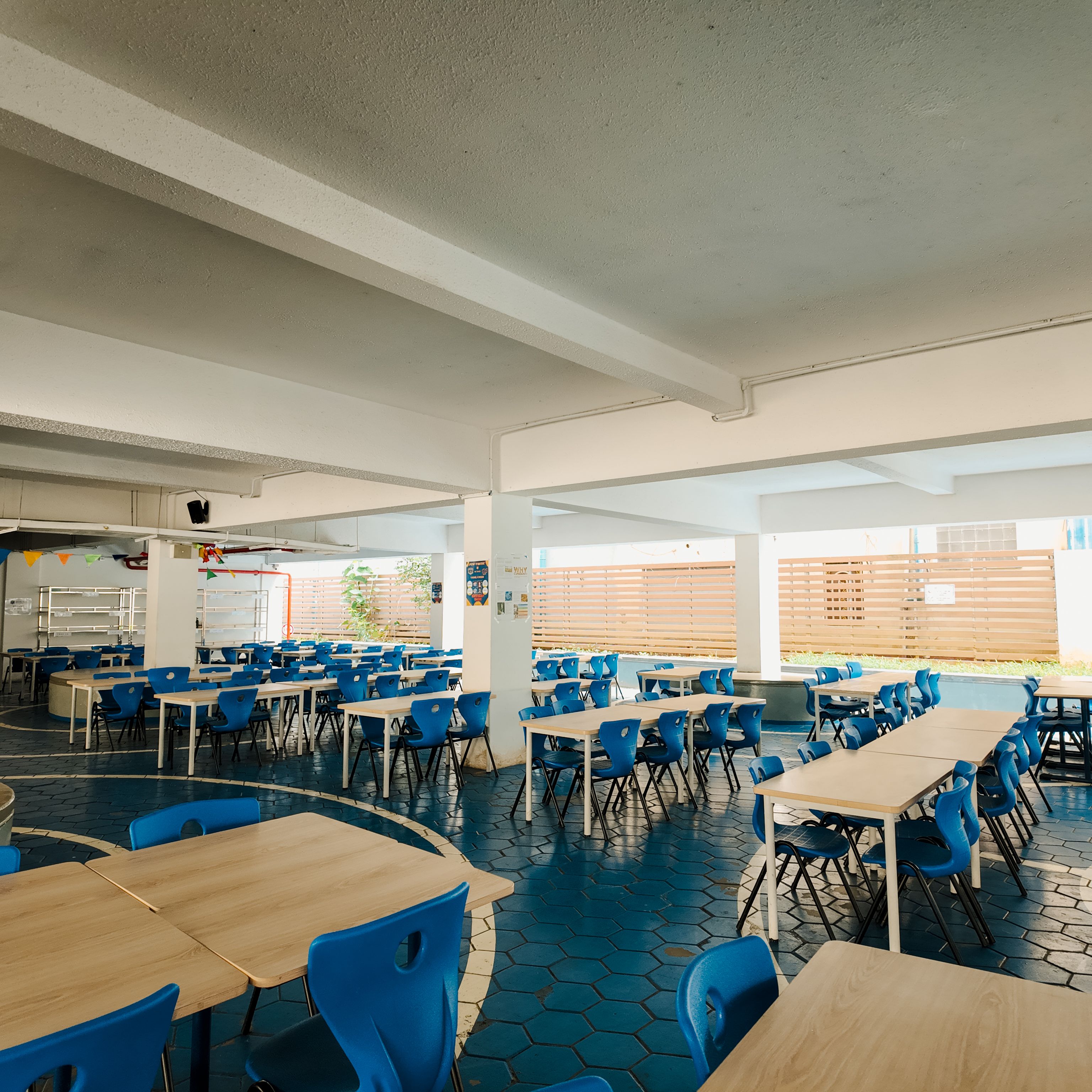 Covered recreational zone at Invictus Phnom Penh with yellow hexagonal floor tiles and table tennis setups, providing shaded space for physical activity and relaxation.