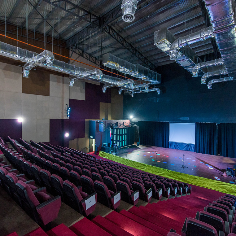 Invictus International School Malaysia Spring Hills Campus auditorium with tiered seating and stage under exposed ductwork