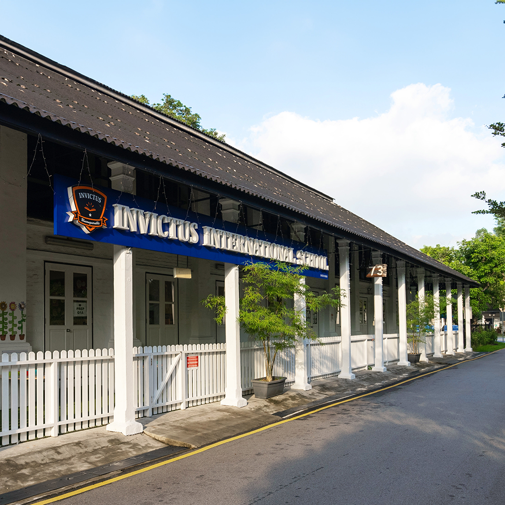 White colonial-style Invictus International School campus building with blue signage and picket fence.