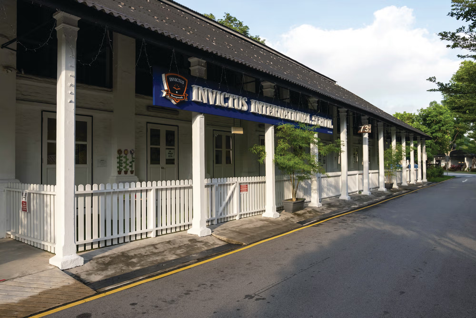 Front view of the Dempsey Hill Invictus International School campus in Singapore, featuring a colonial-style white building with pillars, a school signboard, and a quiet road alongside.