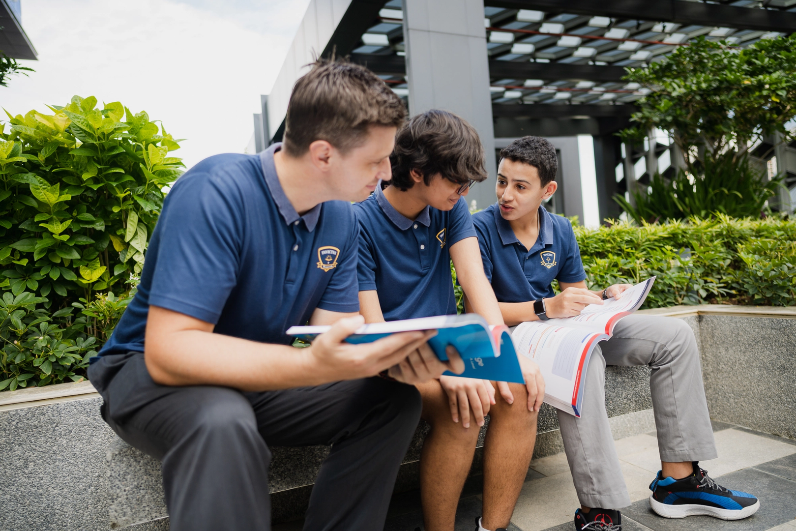 Teacher and two students discussing learning materials outdoors