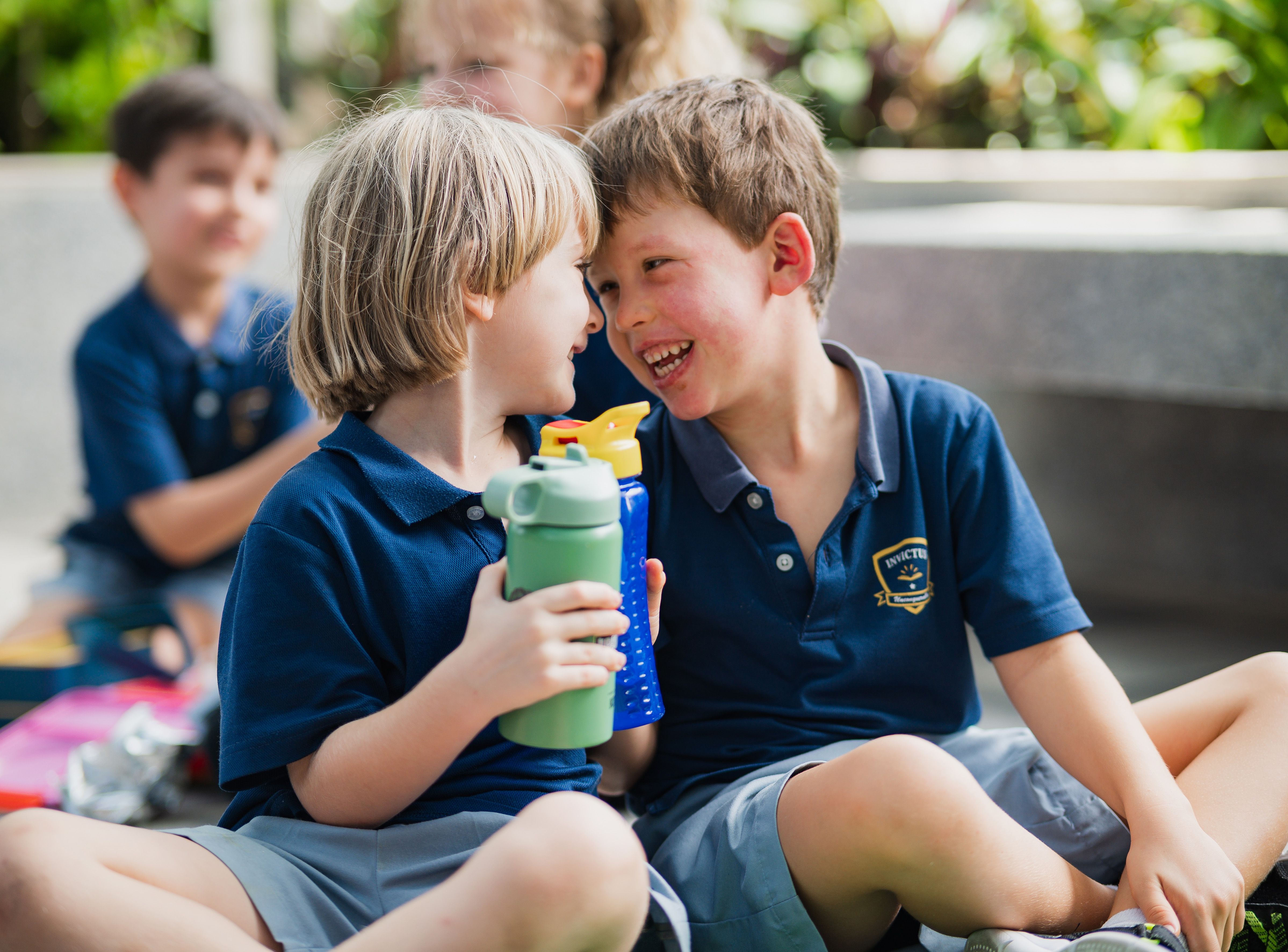 Two kids smiling at each other and holding their water bottles