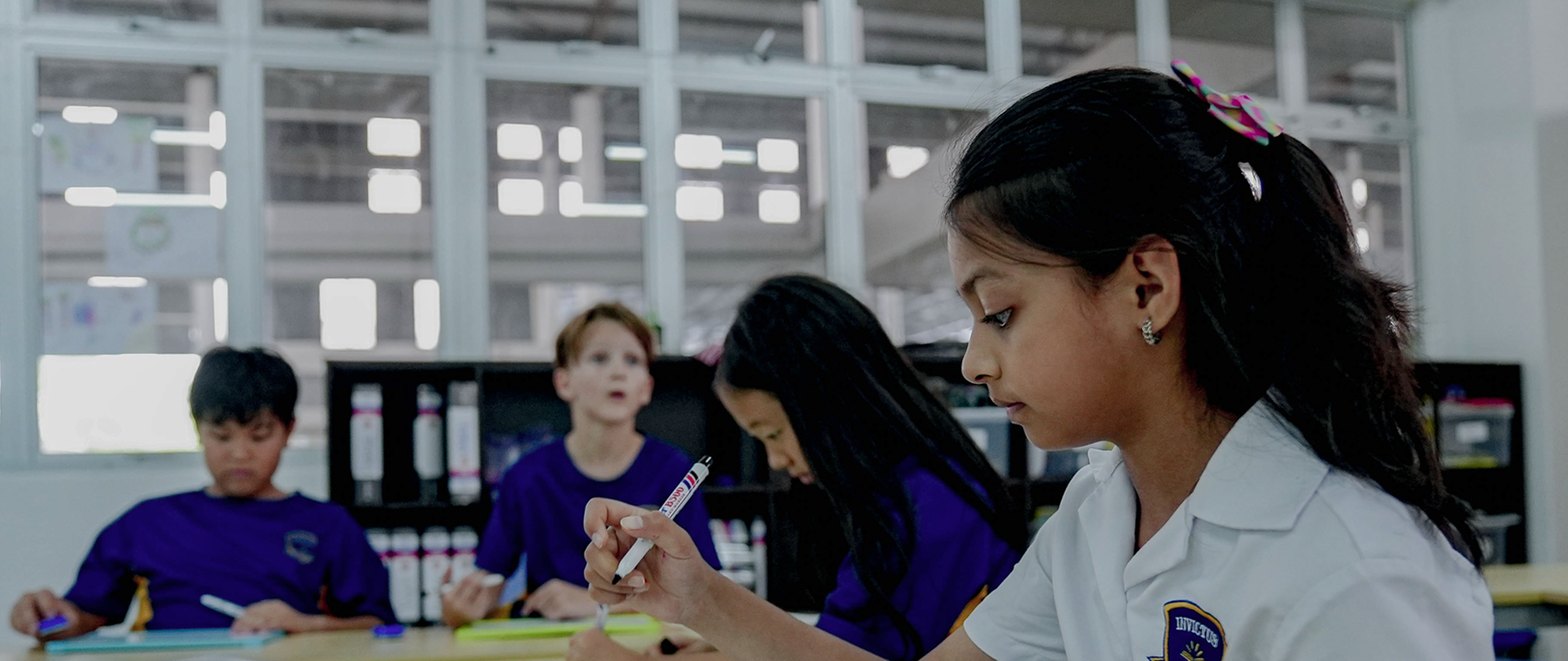 Primary school students at Invictus Spring Hills holding up mini whiteboards to display their answers during a classroom activity.