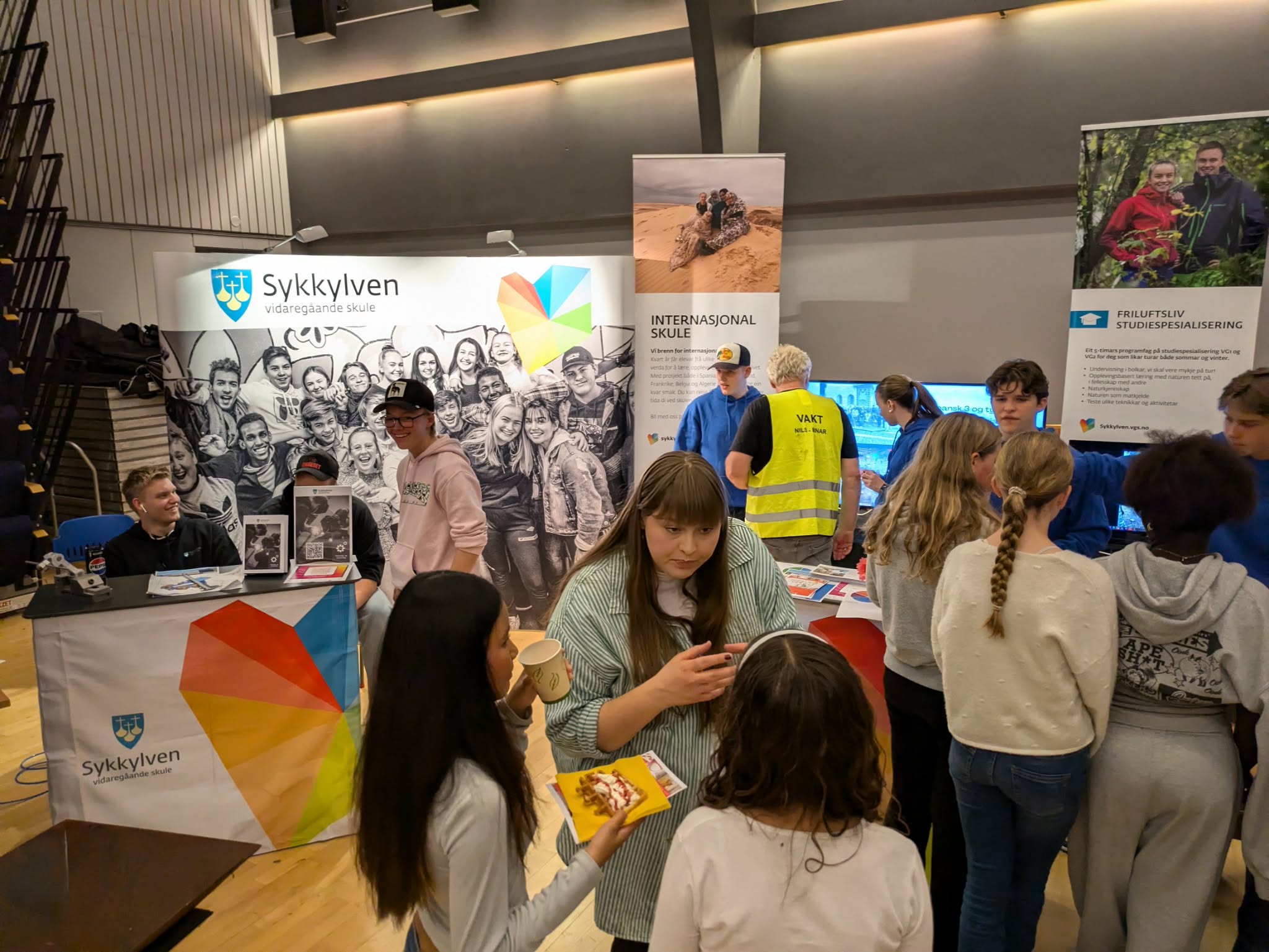 Bilder av ungsom og voksne i engasjert prat, med stand for sykkylven vgs i bakgrunnen