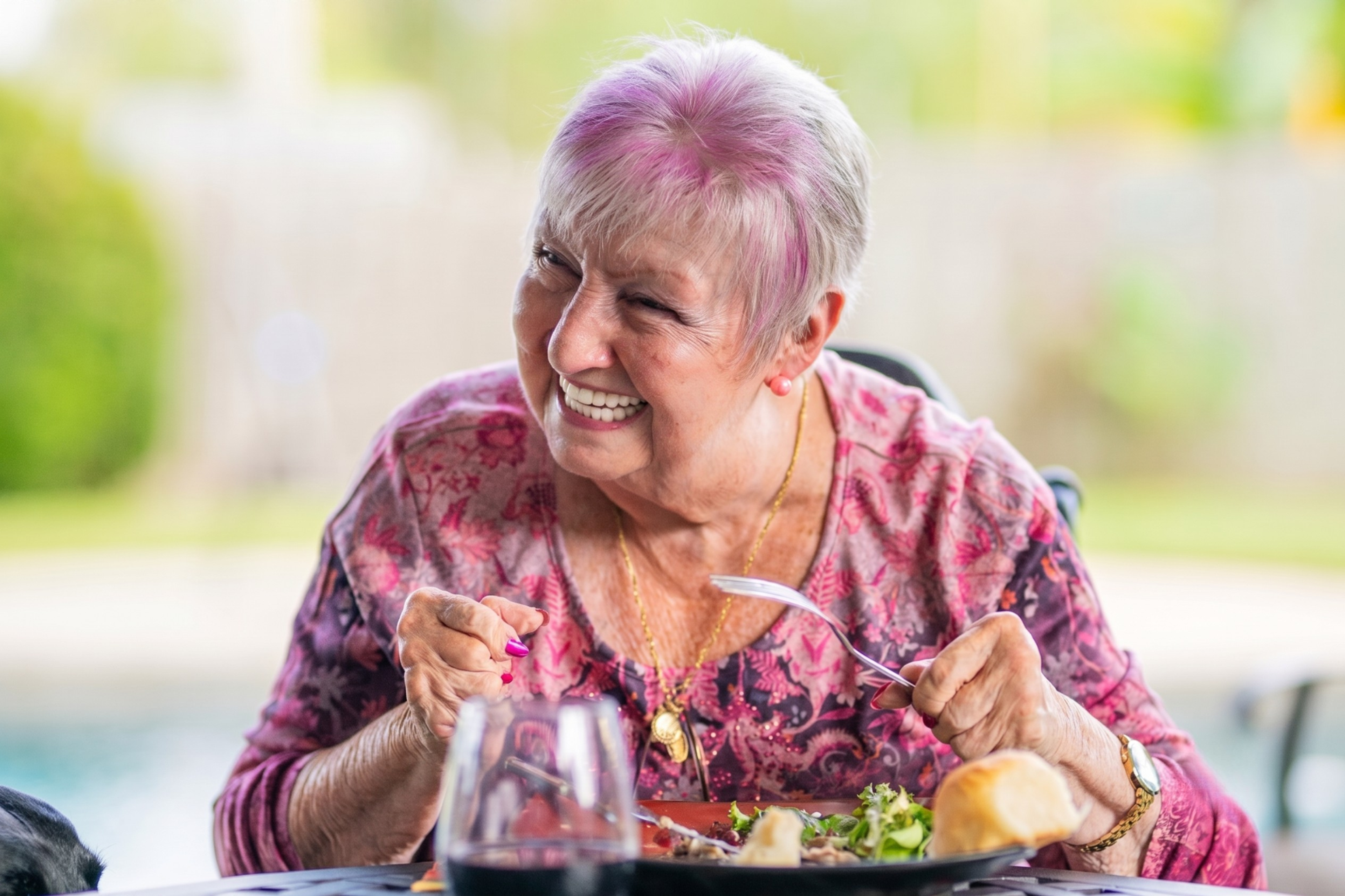 Smiling older woman enjoying a meal comfortably after dental implant treatment in the UK