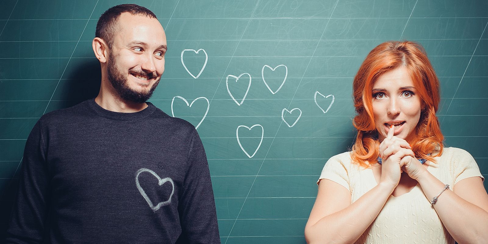 a man and a woman are standing next to each other in front of a blackboard with hearts drawn on it .