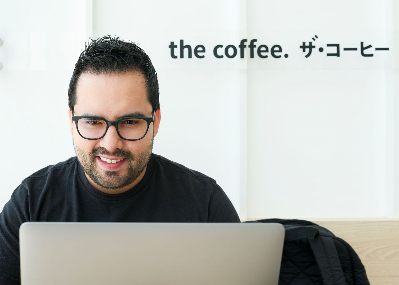 Homem sorrindo enquanto trabalha no notebook, num café
