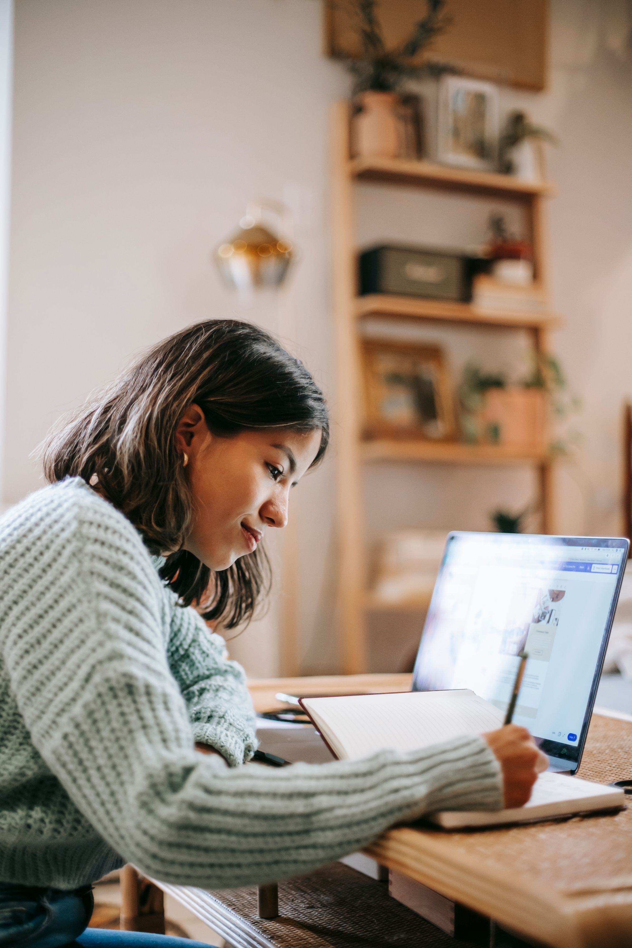 Estudante anotando no caderno, ao lado do notebook, em casa