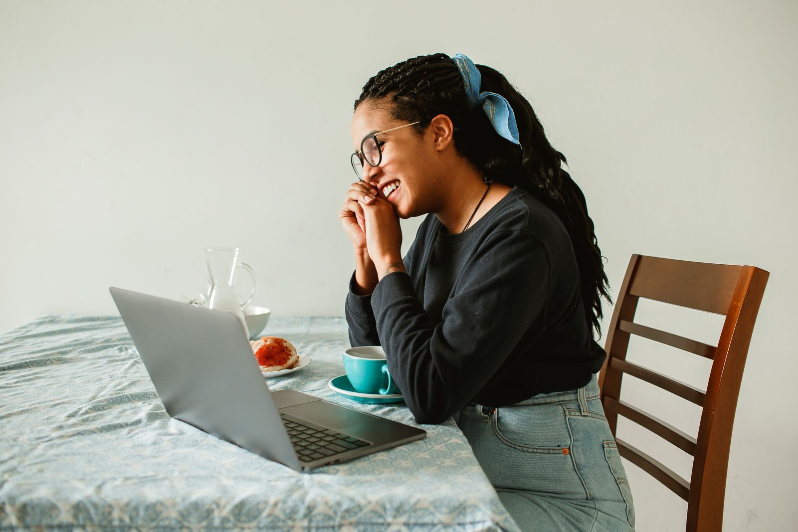 Mulher sorrindo com uma xícara de café, diante do notebook, em casa