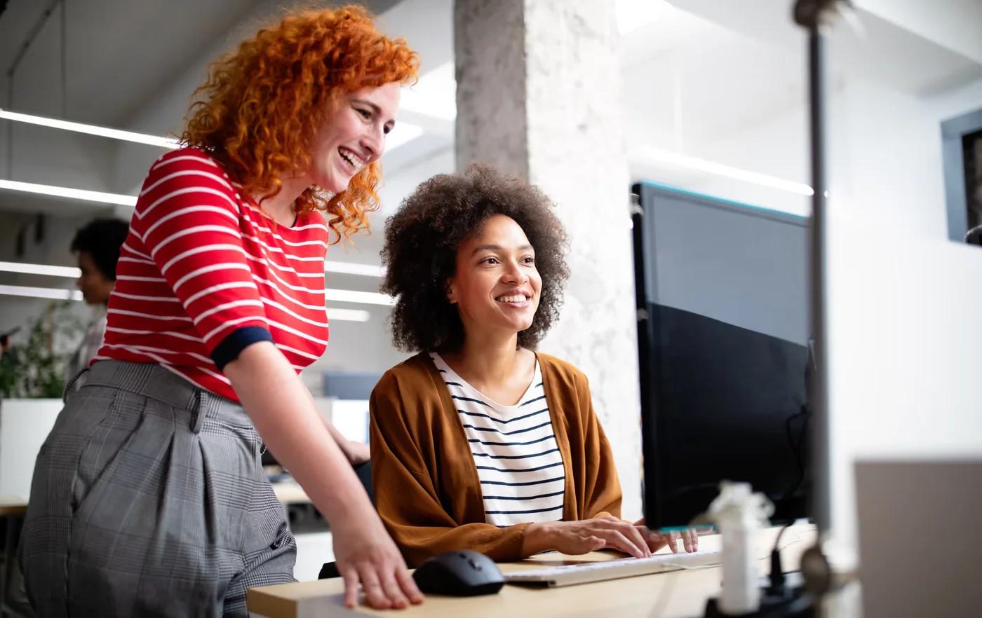 Duas colegas sorrindo diante do computador