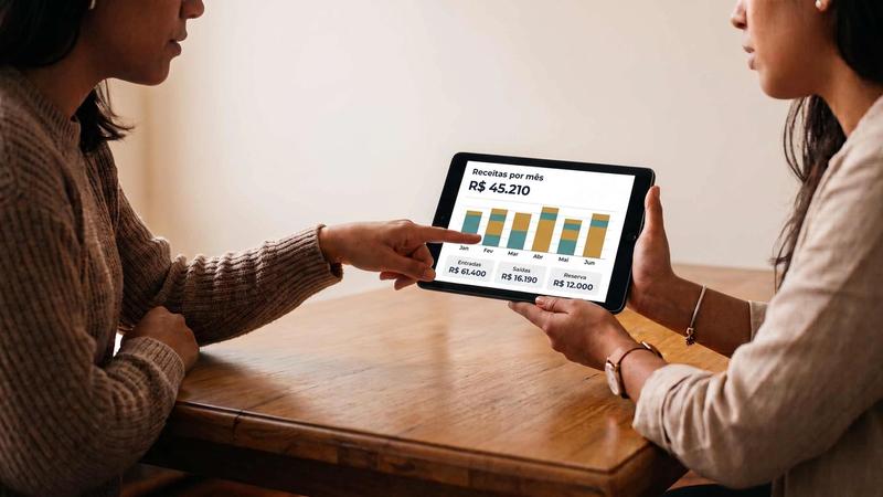 Duas profissionais analisando gráfico de receitas mensais da conta PJ em tablet