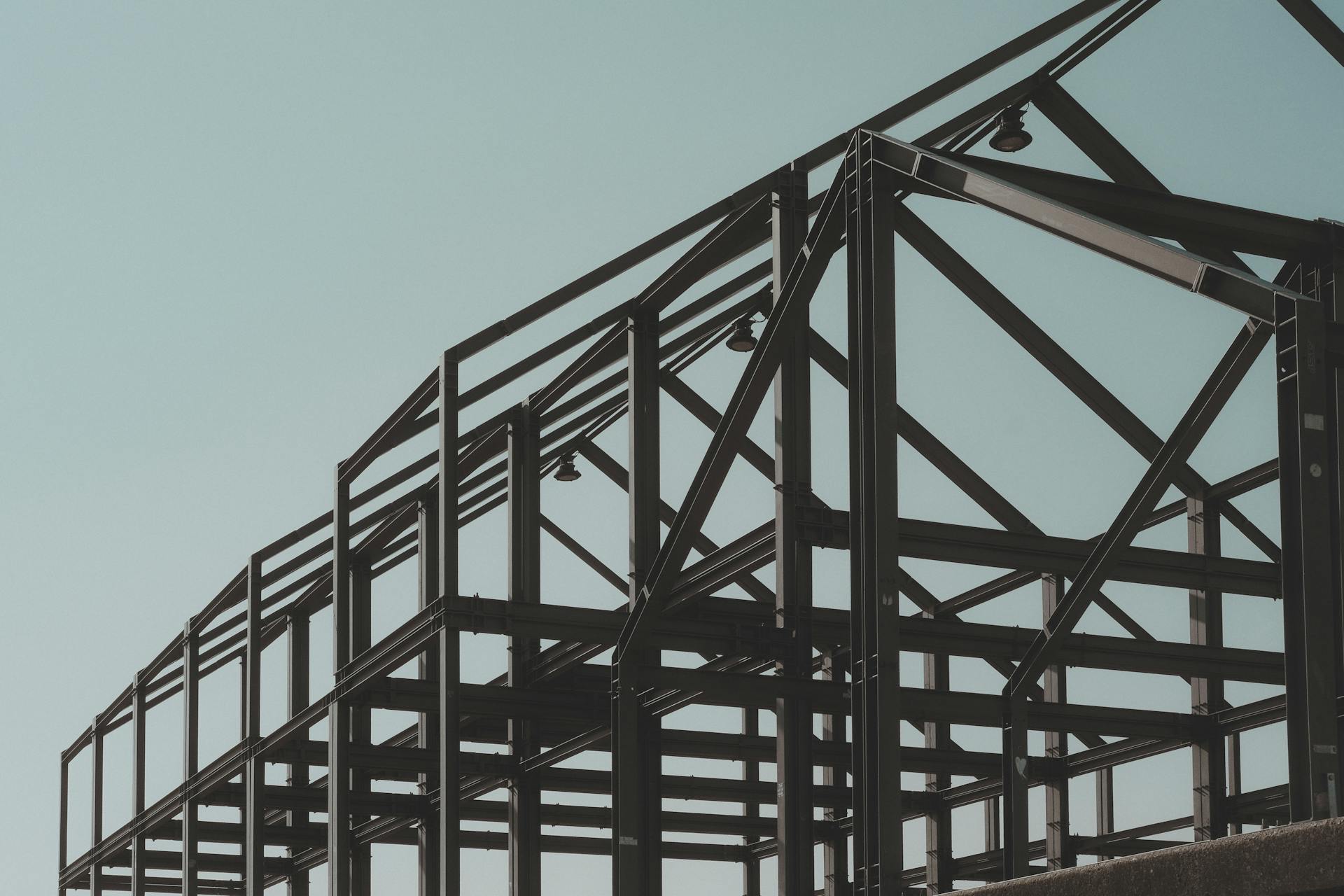 A low-angle photograph of an open structural steel framework against a muted, pale blue sky.
