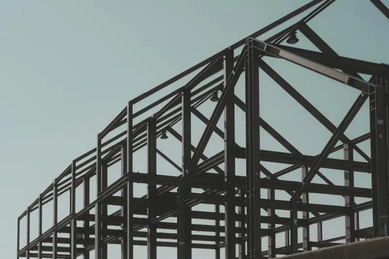 A low-angle photograph of an open structural steel framework against a muted, pale blue sky.