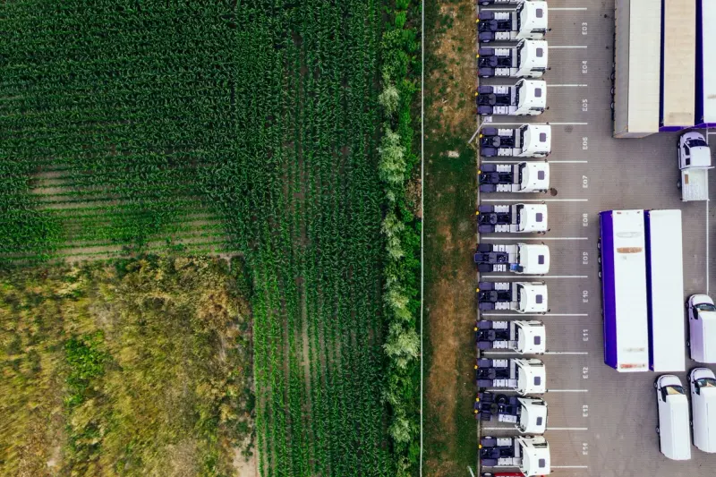 Drone shot of parked trucks next to a lush green cropland