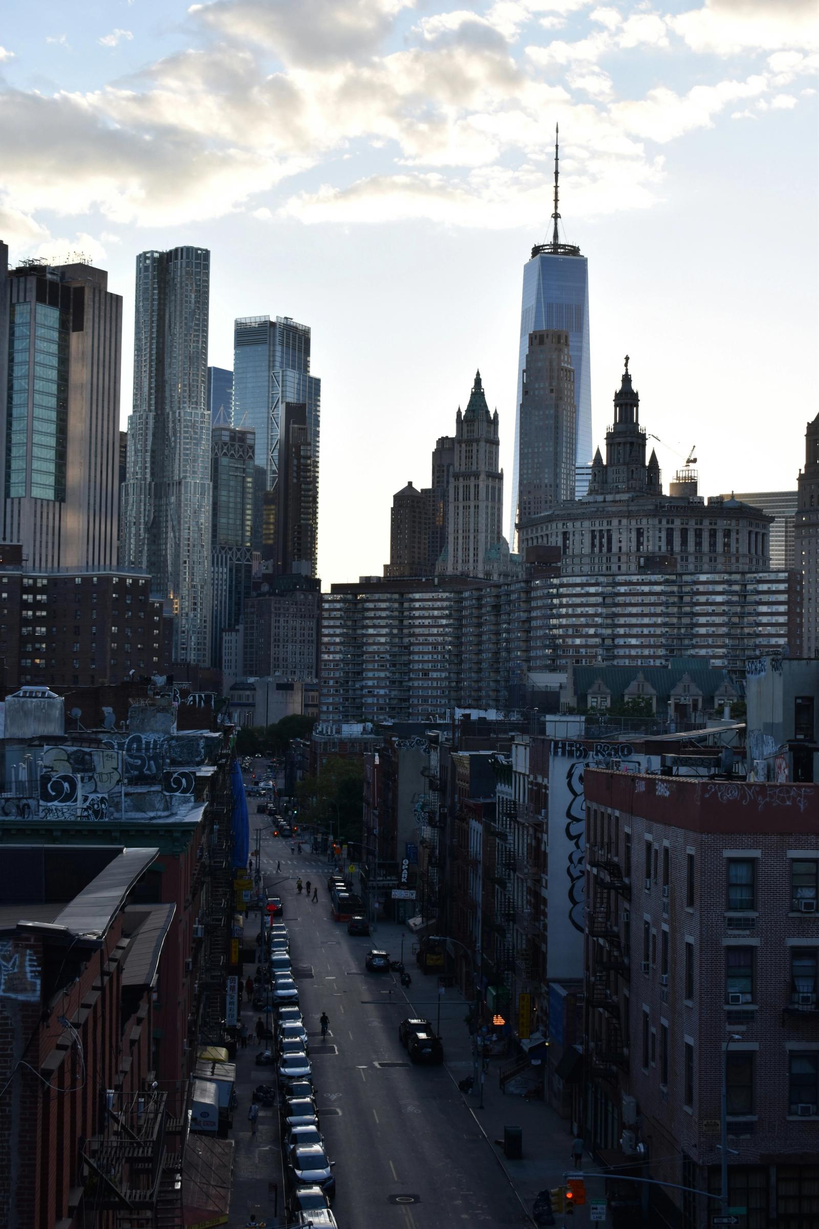 The Lower Manhattan skyline at dusk, One World Trade Center rising above a downtown street