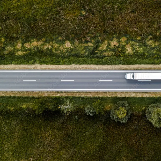 Aerial view of a freight truck travelling a highway between wooded verges