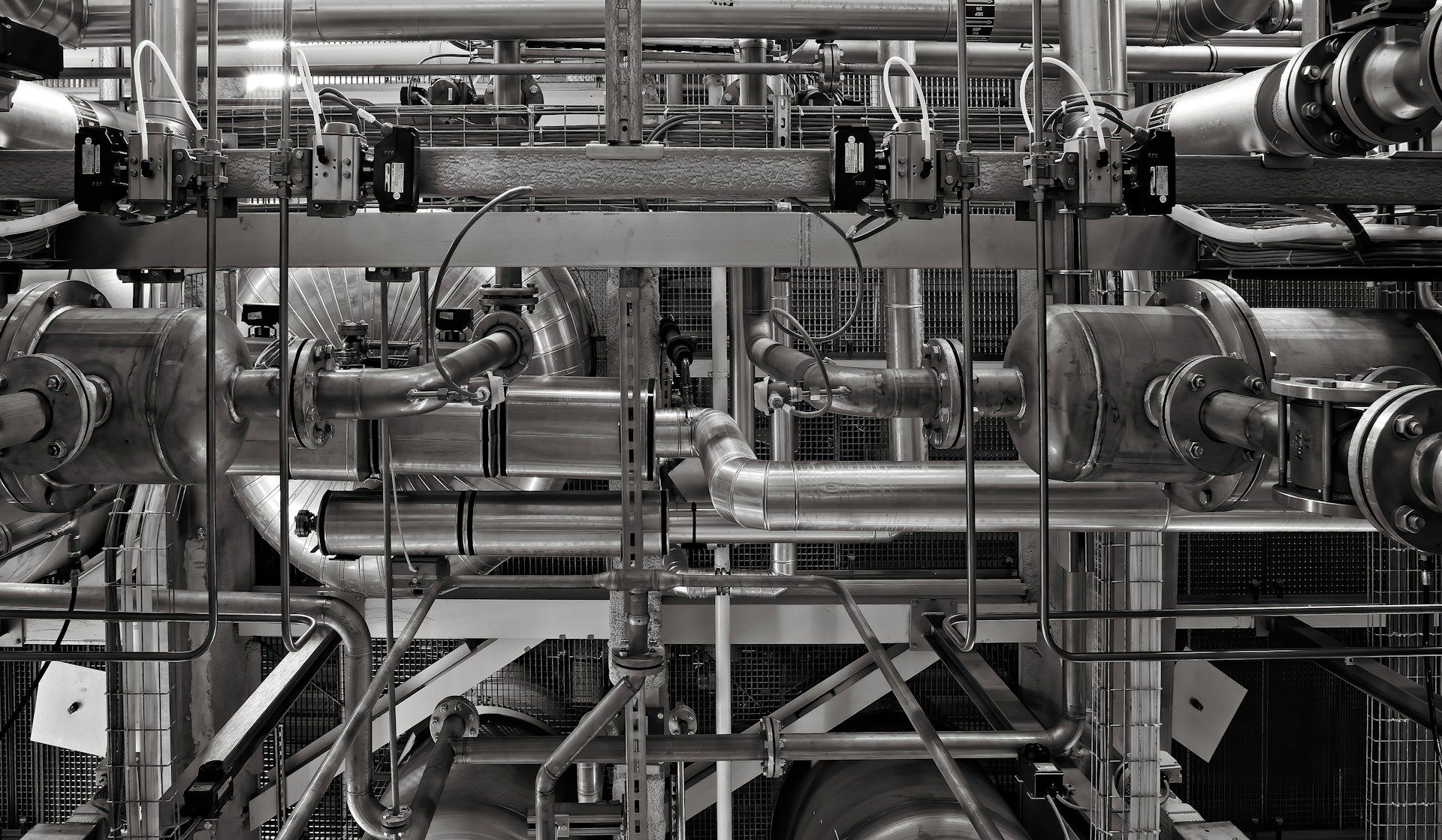 Black and white close-up of industrial pipes, valves and metal scaffolding