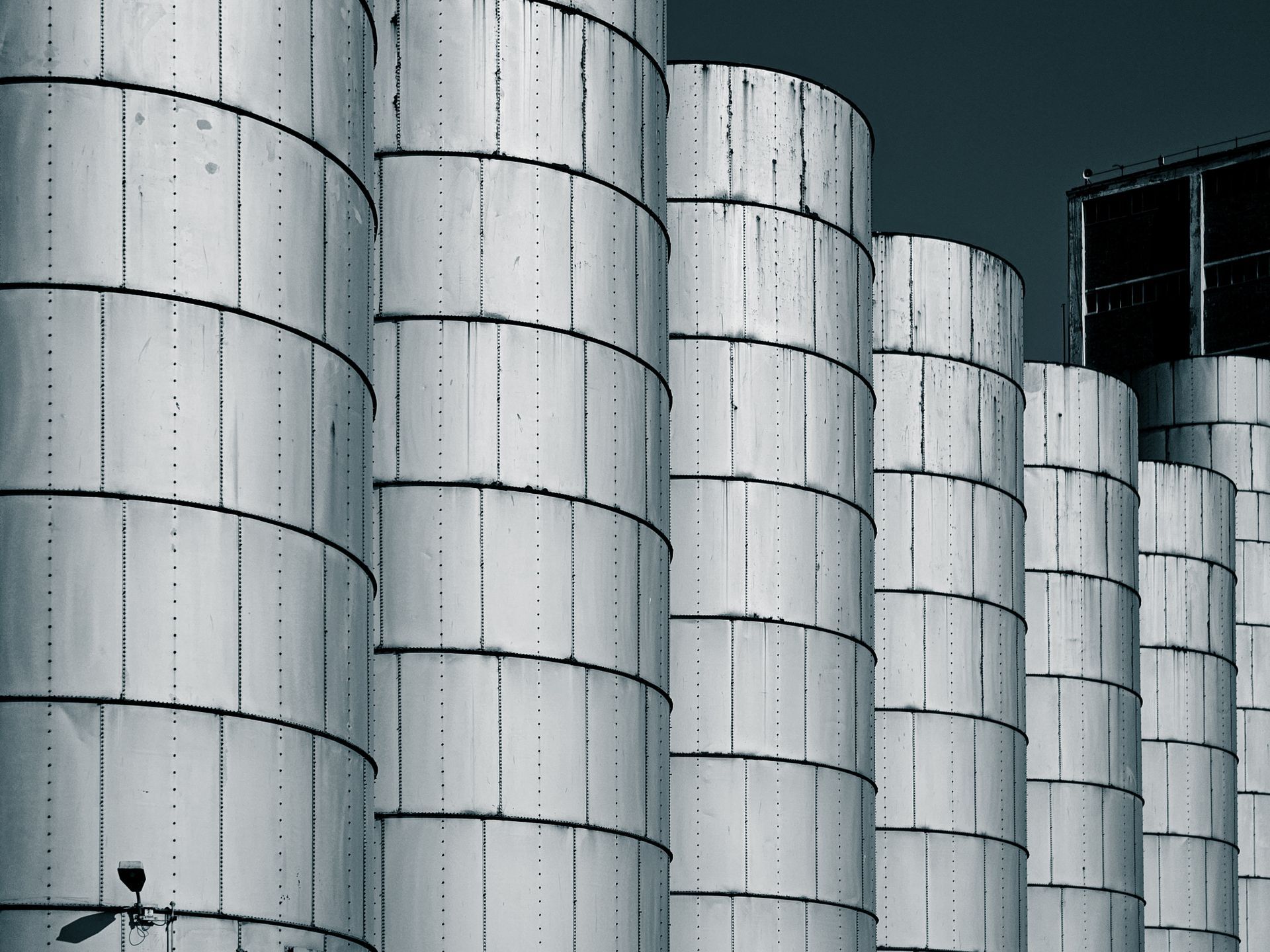 Close-up of industrial metal silos lined up against a dark blue sky, showcasing symmetry.