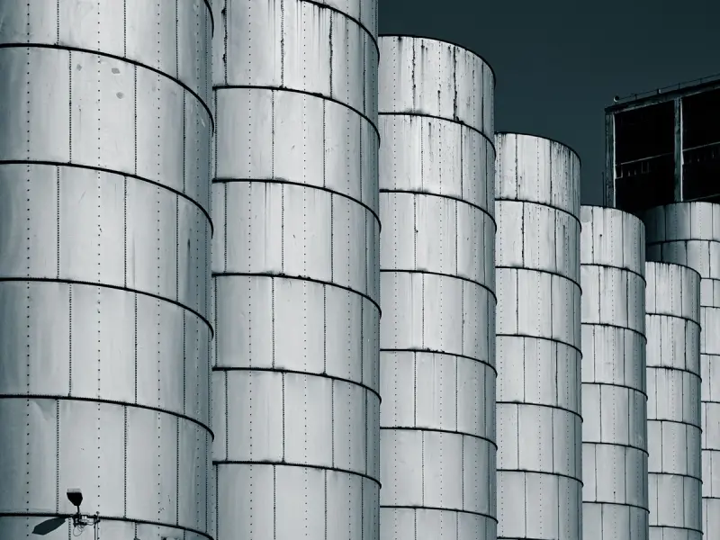 Close-up of industrial metal silos lined up against a dark blue sky, showcasing symmetry.