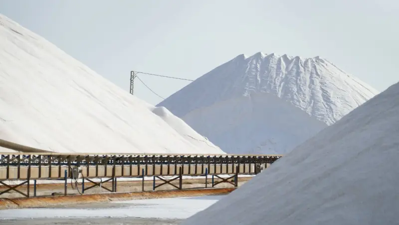 Large mounds of salt with a conveyor belt in an outdoor industrial area.