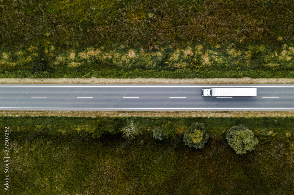 Aerial view of a freight truck travelling a highway between wooded verges