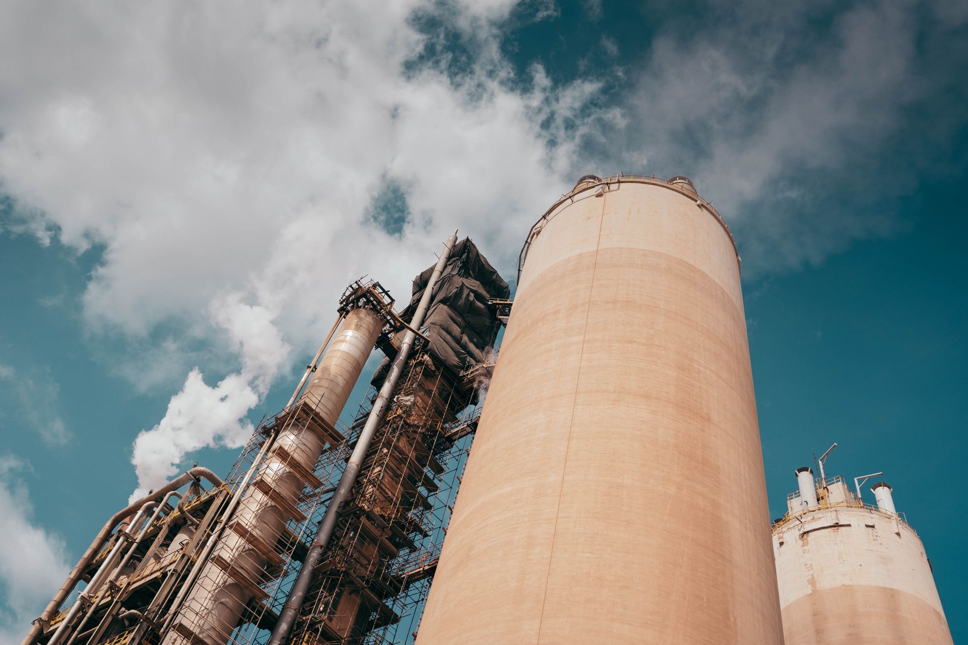 Industrial factory towers emit smoke against a vibrant blue sky, highlighting environmental concerns.