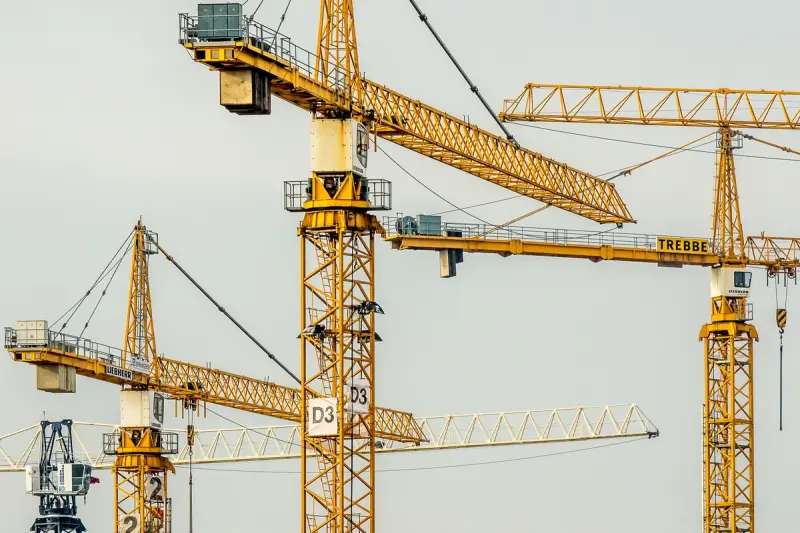 Cluster of yellow tower cranes at a construction site with a gloomy sky background