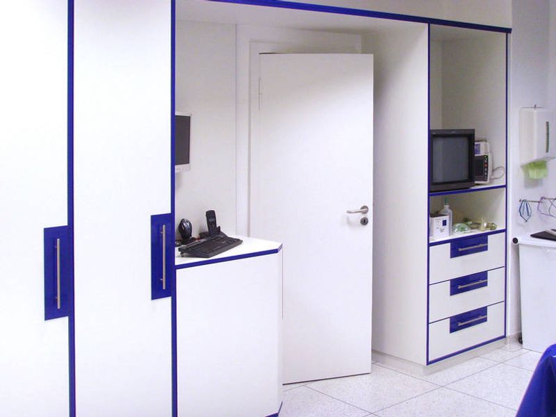 Weiße Einbauschrankwand mit blau abgesetzten Kanten und Schiebetüren in einem Praxisraum