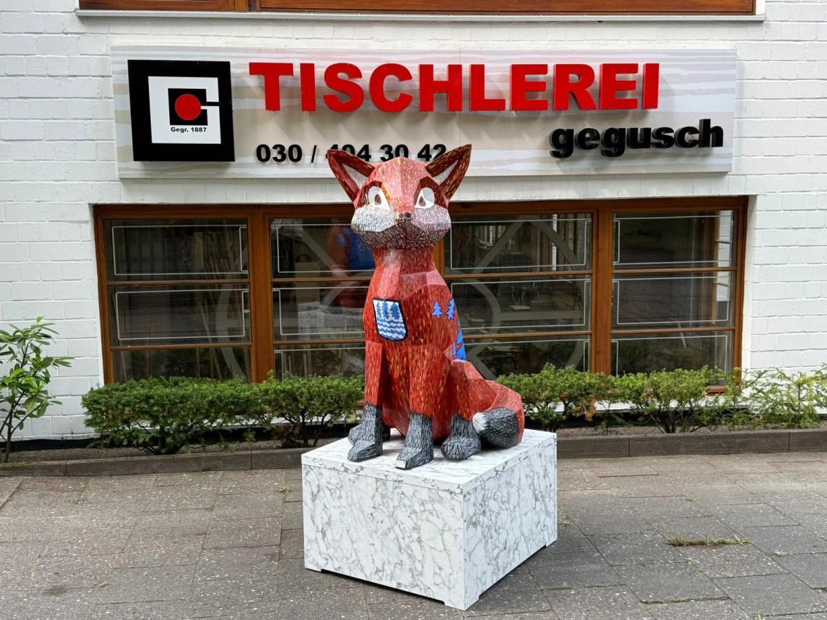 Bunt bemalte Fuchsskulptur der Kampagne #FuchsBezirk auf einem Sockel vor dem Firmenschild der TISCHLEREI gegusch