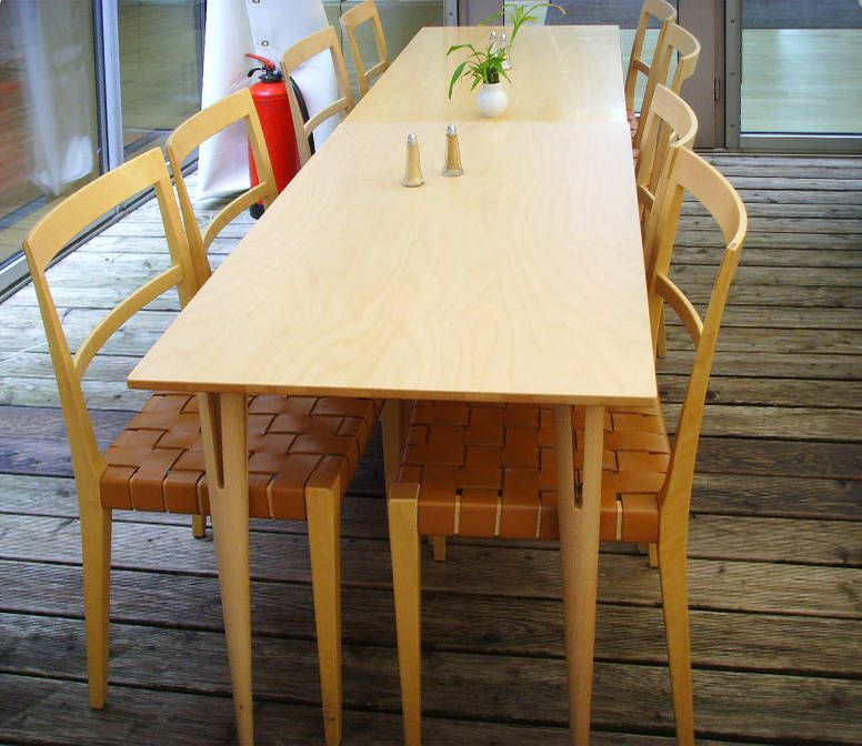 Schmale helle Holztafel mit Stühlen mit geflochtenen Ledersitzen auf einer Holzterrasse