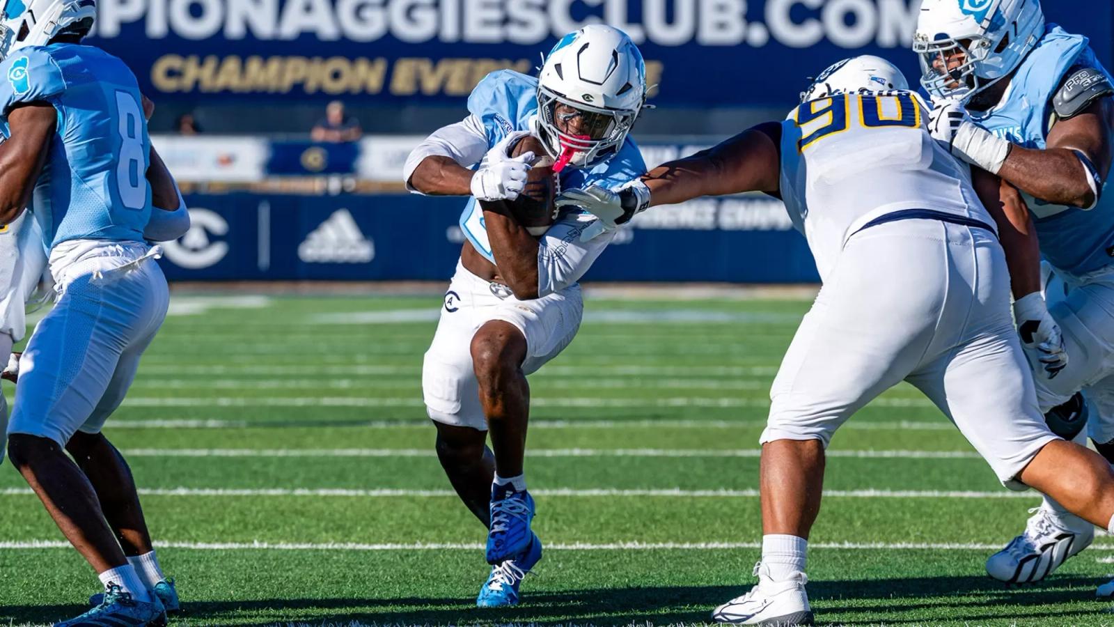 UC Davis running back Jordan Fisher carries the ball as a Northern Colorado defender wearing No. 90 reaches for the tackle at UC Davis Health Stadium