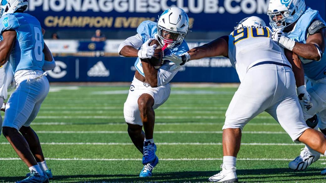 UC Davis running back Jordan Fisher carries the ball as a Northern Colorado defender wearing No. 90 reaches for the tackle at UC Davis Health Stadium