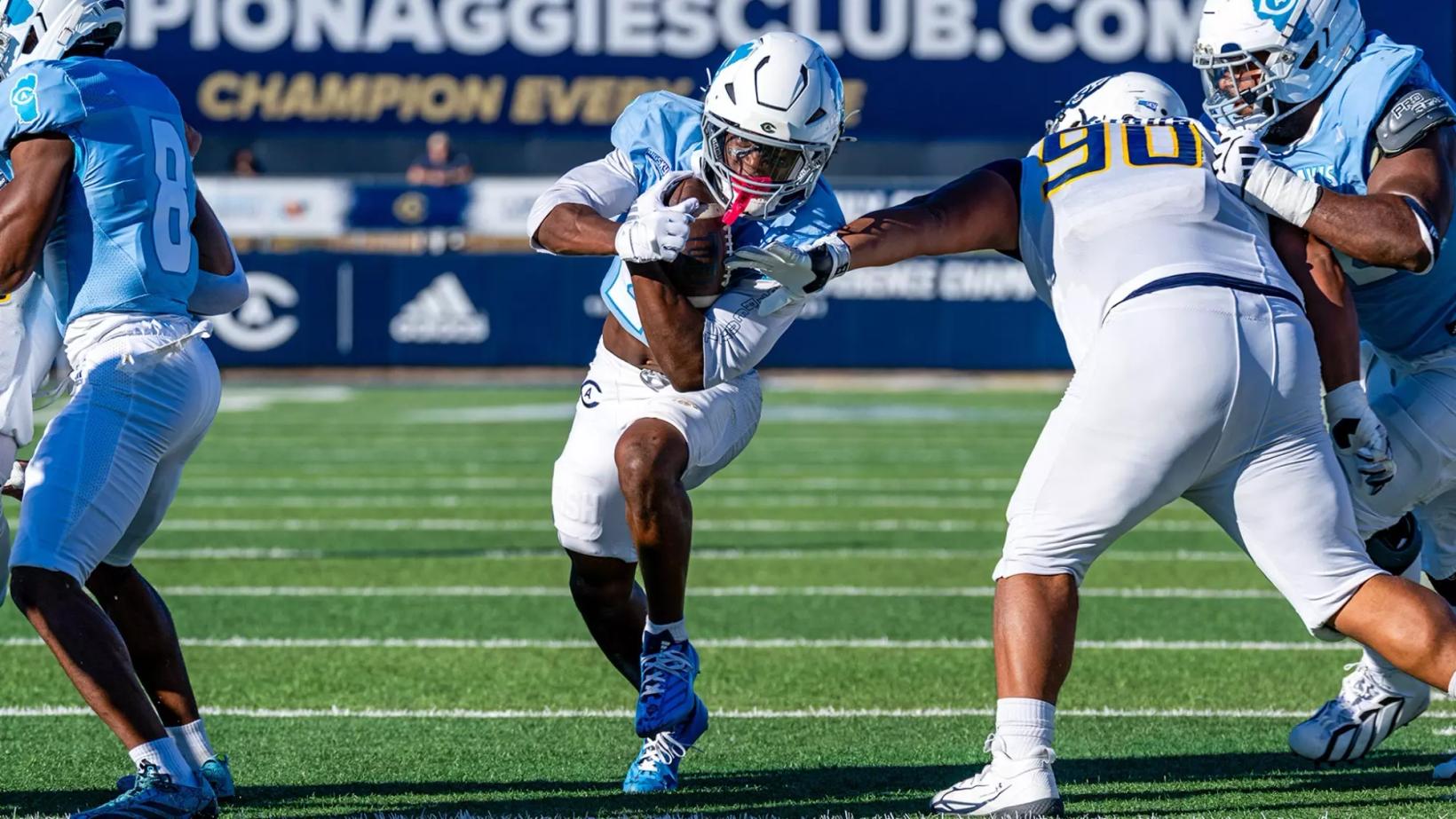 UC Davis running back Jordan Fisher carries the ball as a Northern Colorado defender wearing No. 90 reaches for the tackle at UC Davis Health Stadium