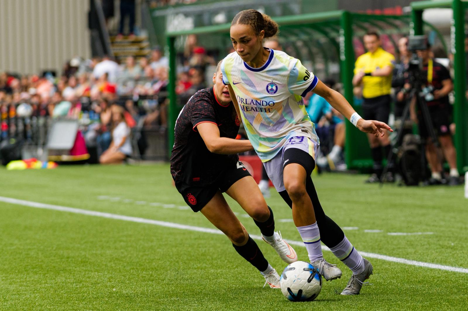 An Orlando Pride attacker in the white Orlando Health kit shields the ball from a Portland Thorns defender near the sideline during the August 15, 2026 match at Providence Park.