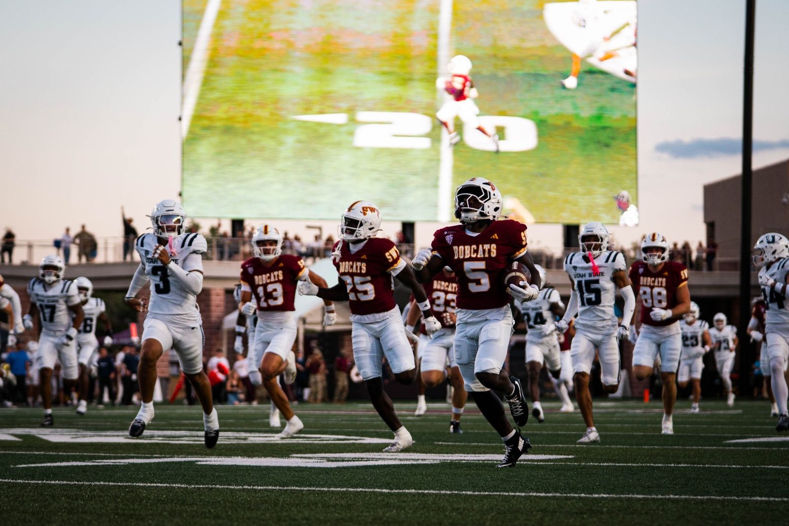 Texas State running back Jaylen Jenkins (5), in a maroon Bobcats jersey, runs upfield with the ball as teammates and Utah State players in white give chase at UFCU Stadium during Texas State's 20-17 win on Oct. 24, 2026