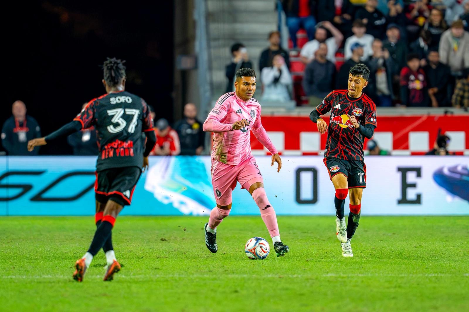 A Red Bull New York player in black and red carries the ball past an Inter Miami player in pink at Sports Illustrated Stadium on October 24, 2026.