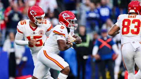 Kansas City Chiefs quarterback Patrick Mahomes, wearing No. 15, hands the ball to running back Kenneth Walker III, wearing No. 9, as a teammate wearing No. 83 moves ahead of them.