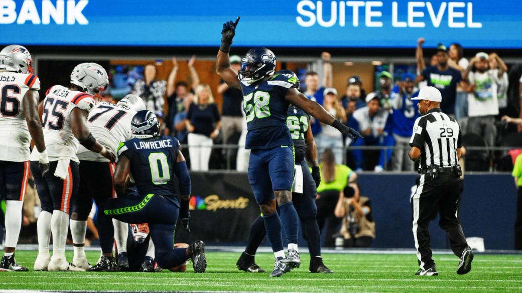 Seattle Seahawks' Derick Hall (58) raises a finger to celebrate as teammate DeMarcus Lawrence (0) kneels on the turf near several New England Patriots players at Lumen Field.