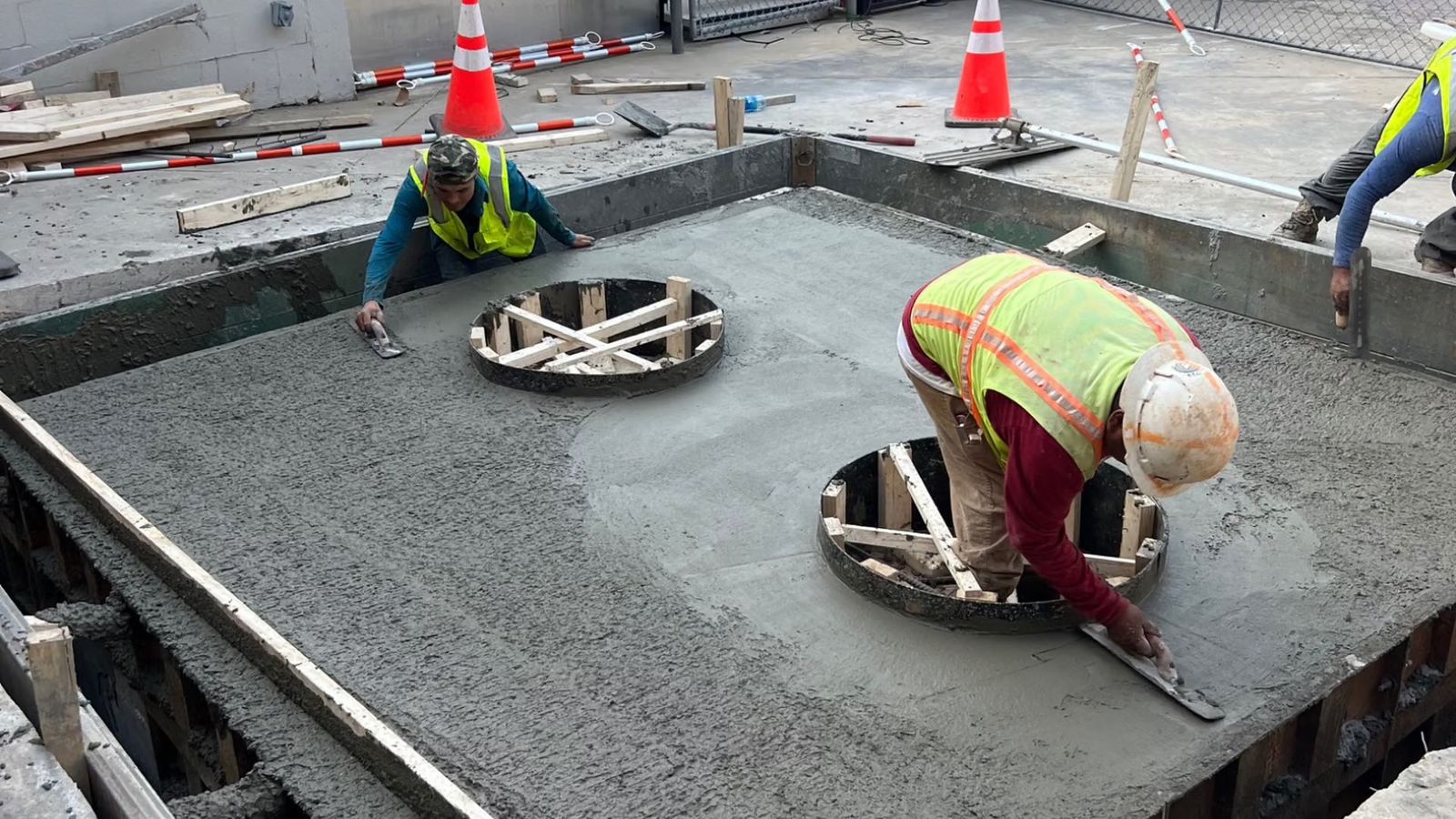 Construction workers finish a fresh concrete slab poured around two circular access openings