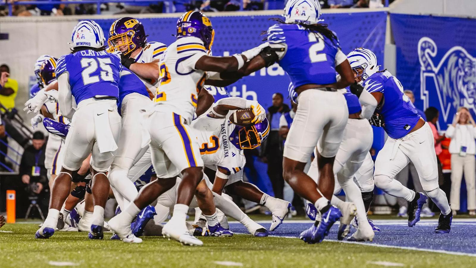 An East Carolina ball carrier in a white jersey, No. 3, reaches the ball toward the goal line in a pile of Memphis defenders in blue jerseys during ECU's 41-34 overtime loss at Simmons Bank Liberty Stadium on Oct. 22, 2026.