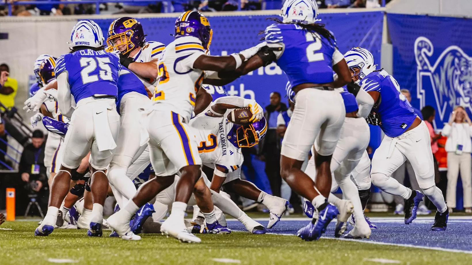 An East Carolina ball carrier in a white jersey, No. 3, reaches the ball toward the goal line in a pile of Memphis defenders in blue jerseys during ECU's 41-34 overtime loss at Simmons Bank Liberty Stadium on Oct. 22, 2026.