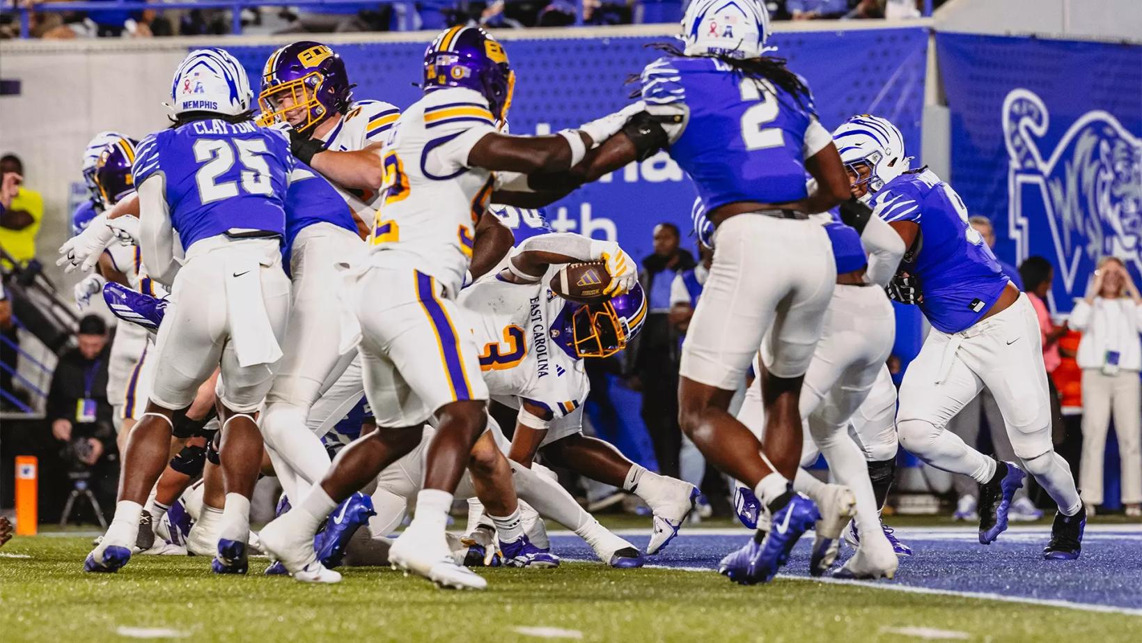 An East Carolina ball carrier in a white jersey, No. 3, reaches the ball toward the goal line in a pile of Memphis defenders in blue jerseys during ECU's 41-34 overtime loss at Simmons Bank Liberty Stadium on Oct. 22, 2026.