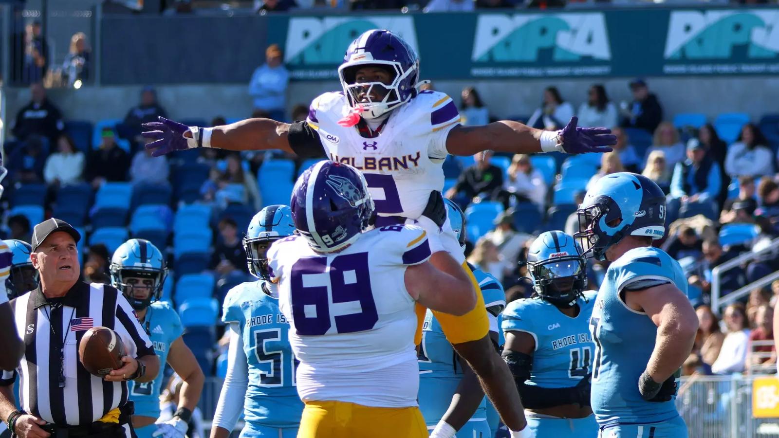 A UAlbany player is lifted in celebration by teammate No. 69 in front of Rhode Island defenders at Centreville Bank Stadium