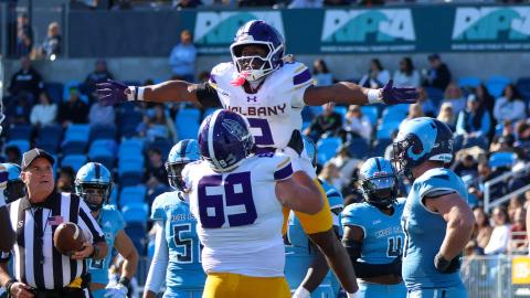 A UAlbany player is lifted in celebration by teammate No. 69 in front of Rhode Island defenders at Centreville Bank Stadium