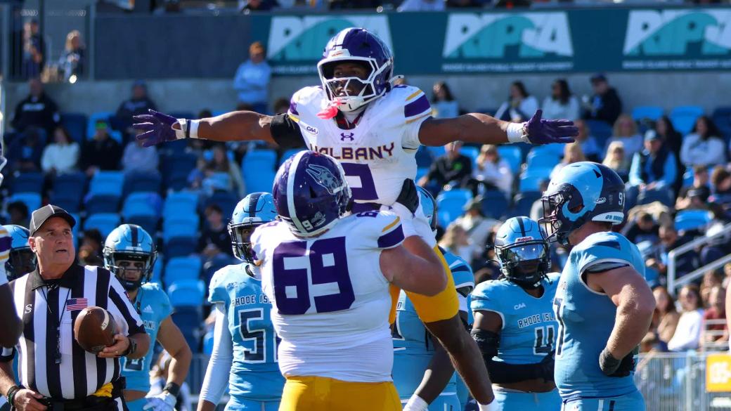 A UAlbany player is lifted in celebration by teammate No. 69 in front of Rhode Island defenders at Centreville Bank Stadium