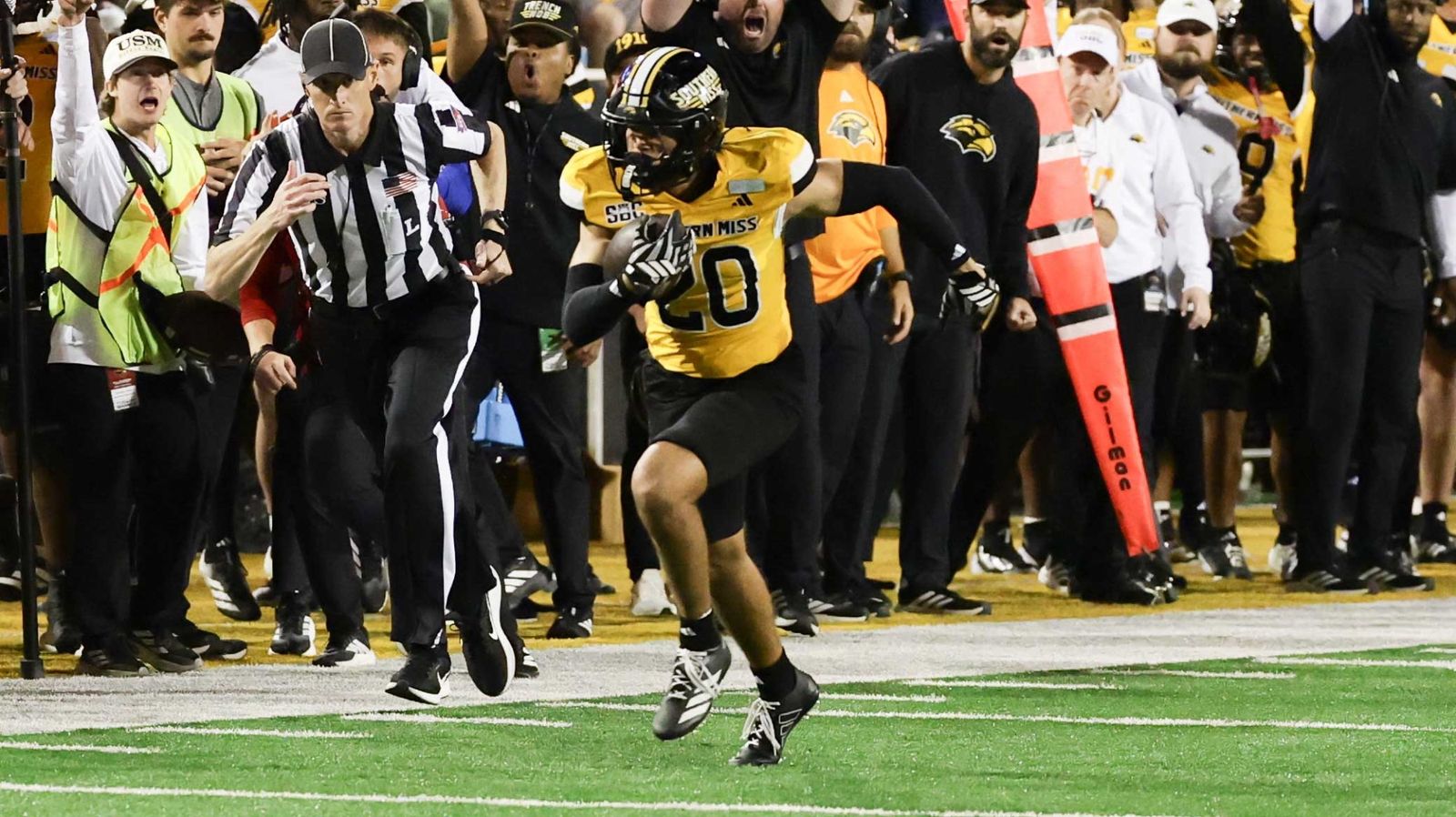 Southern Miss player No. 20 in a gold jersey runs with the ball along the sideline as coaches and teammates react during the Golden Eagles' 35-31 homecoming win over Louisiana at Renasant Stadium on Oct. 24, 2026