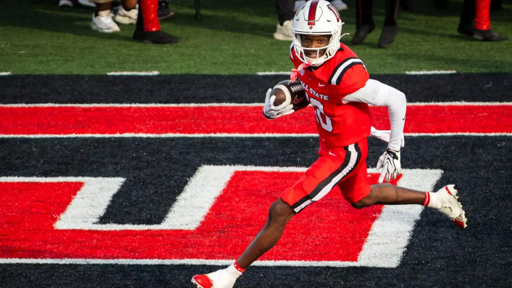 Ball State's No. 10, in a red uniform and white helmet, carries the ball through the end zone during the homecoming game against Sacramento State at Scheumann Stadium on Oct. 24, 2026.