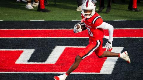 Ball State's No. 10, in a red uniform and white helmet, carries the ball through the end zone during the homecoming game against Sacramento State at Scheumann Stadium on Oct. 24, 2026.