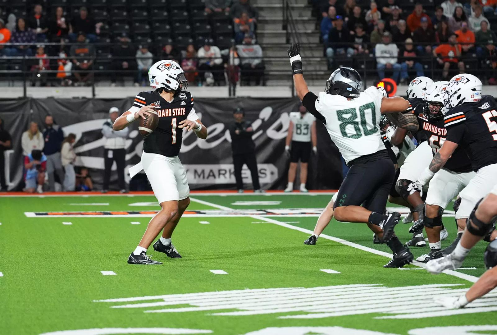 Idaho State quarterback Jordan Cooke, No. 1 in black, sets to pass as a Portland State defender in a white No. 80 jersey rushes inside the ICCU Dome in Pocatello, Oct. 24, 2026