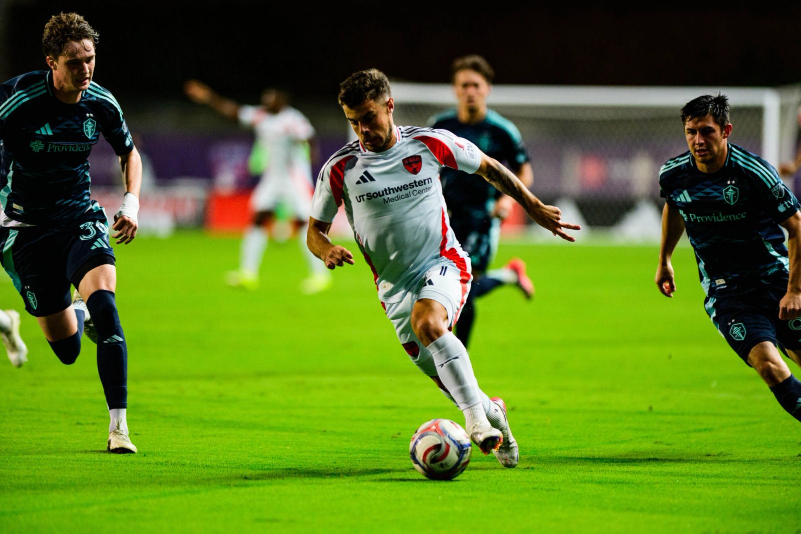 FC Dallas player dribbles past Seattle Sounders players at Toyota Stadium